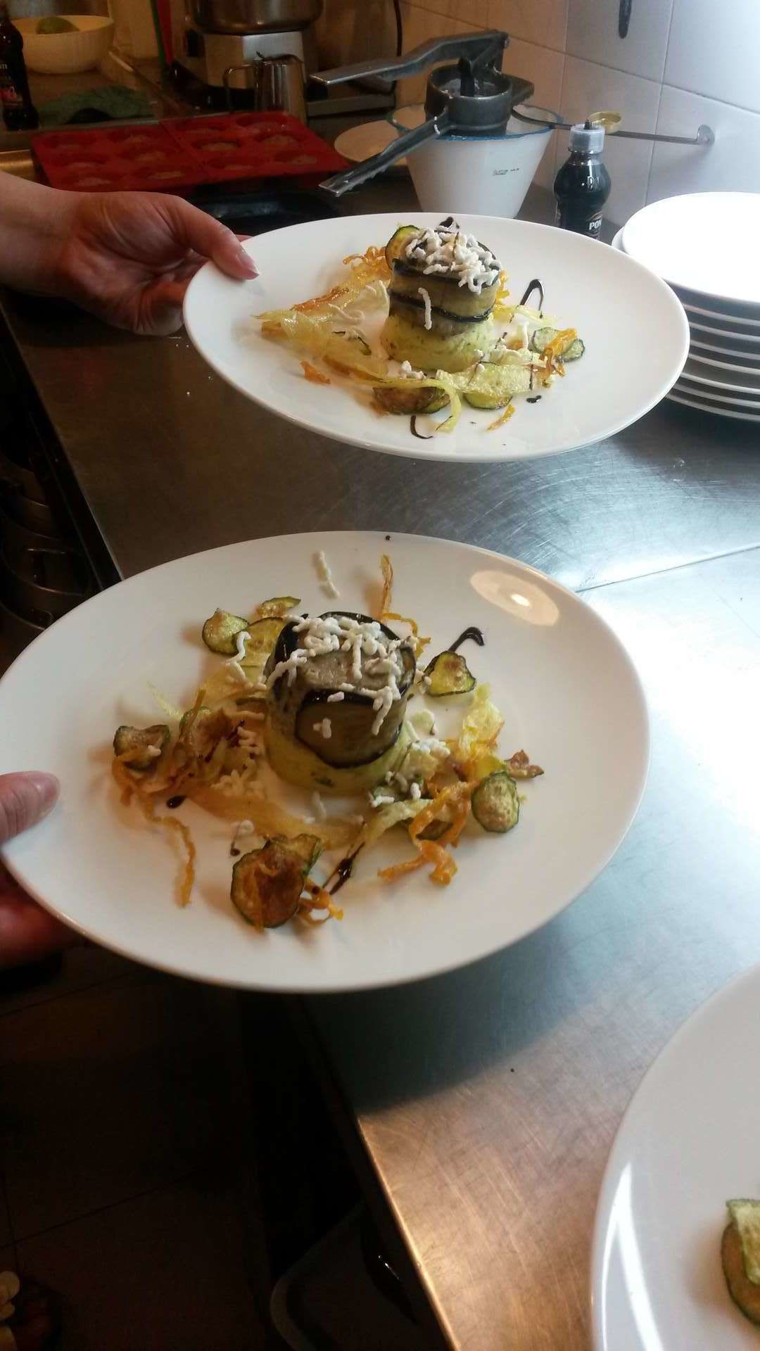 Dos platos blancos con un guiso de verduras rellenas y queso rallado, sostenidos por una persona.