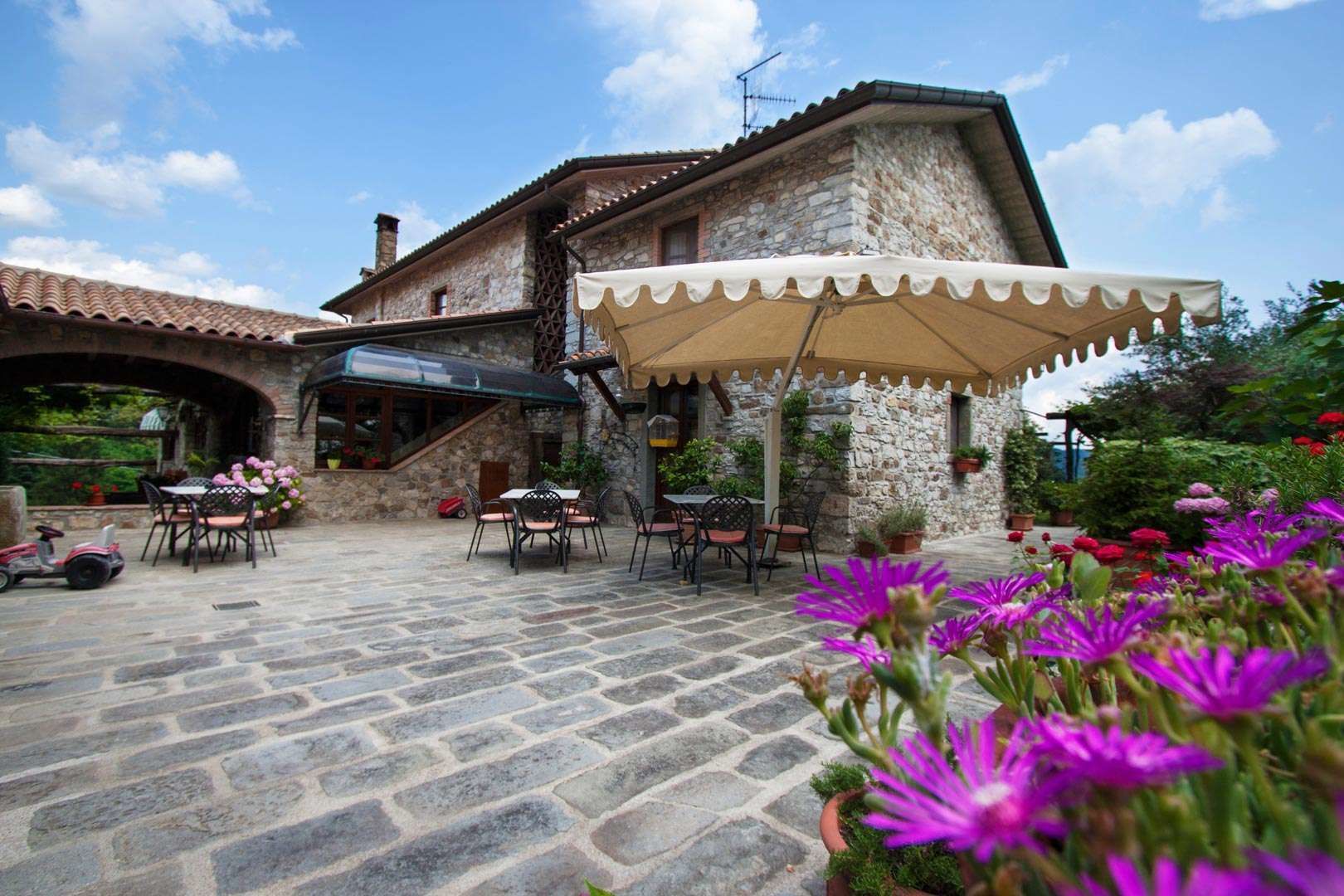 Ein Gebäude aus Stein mit einer Terrasse, Sitzgelegenheiten und Pflanzen in Töpfen.