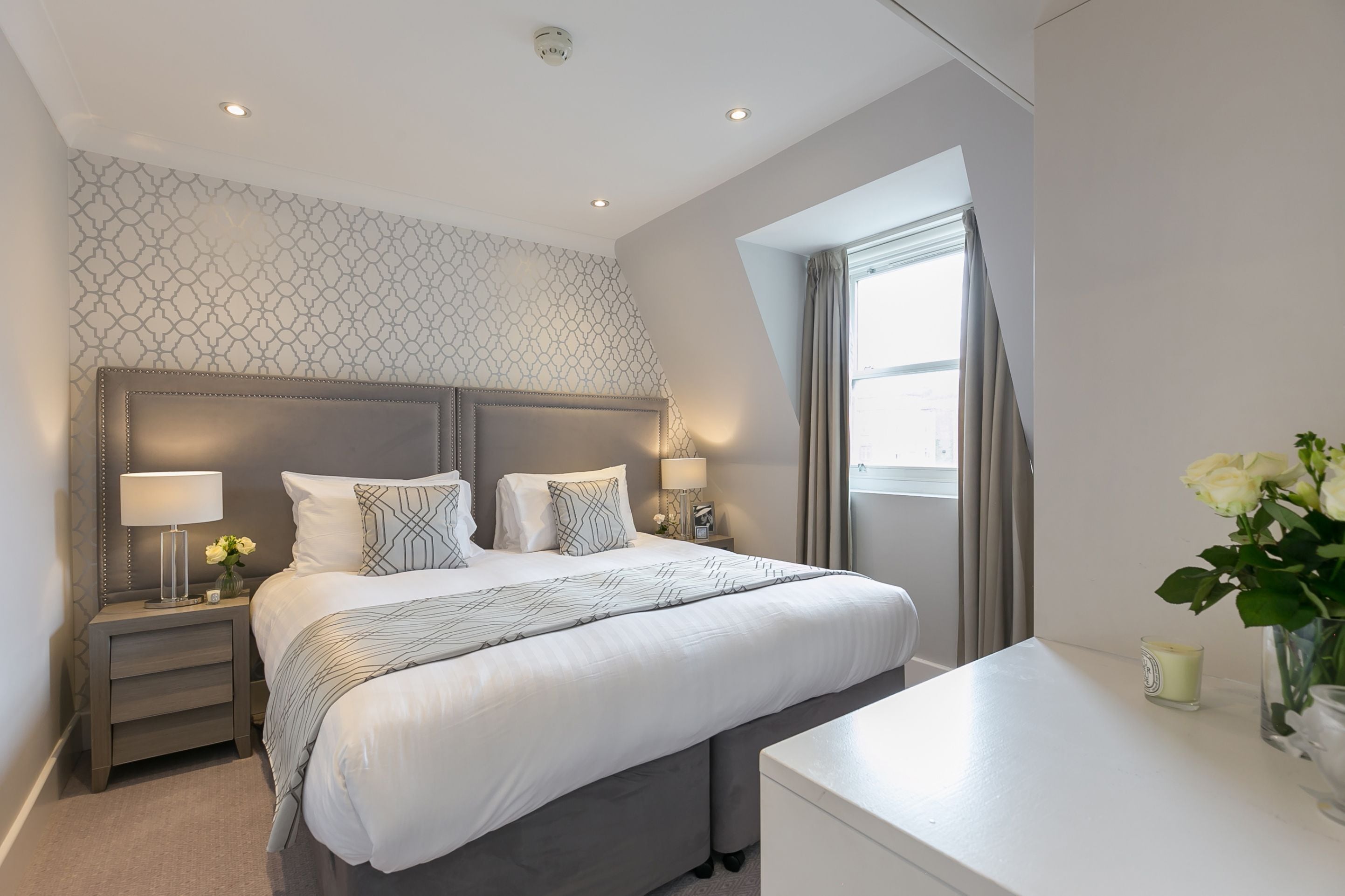 Een moderne hotelkamer met een groot bed, nachtkastjes, een bureau en een raam met gordijnen.