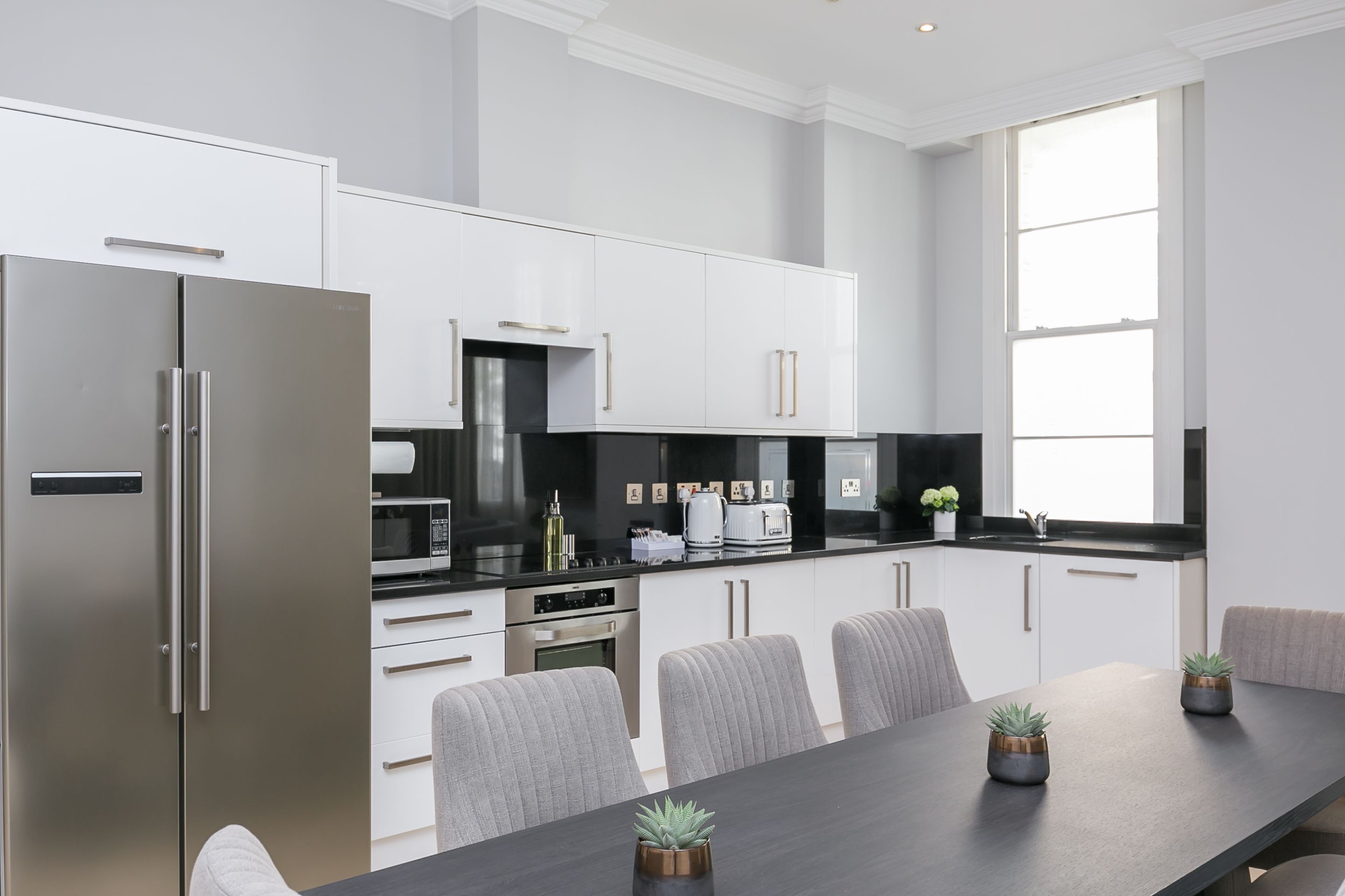 Una cucina moderna con mobili bianchi, elettrodomestici in acciaio inossidabile e una zona pranzo con sedie grigie e un tavolo scuro.