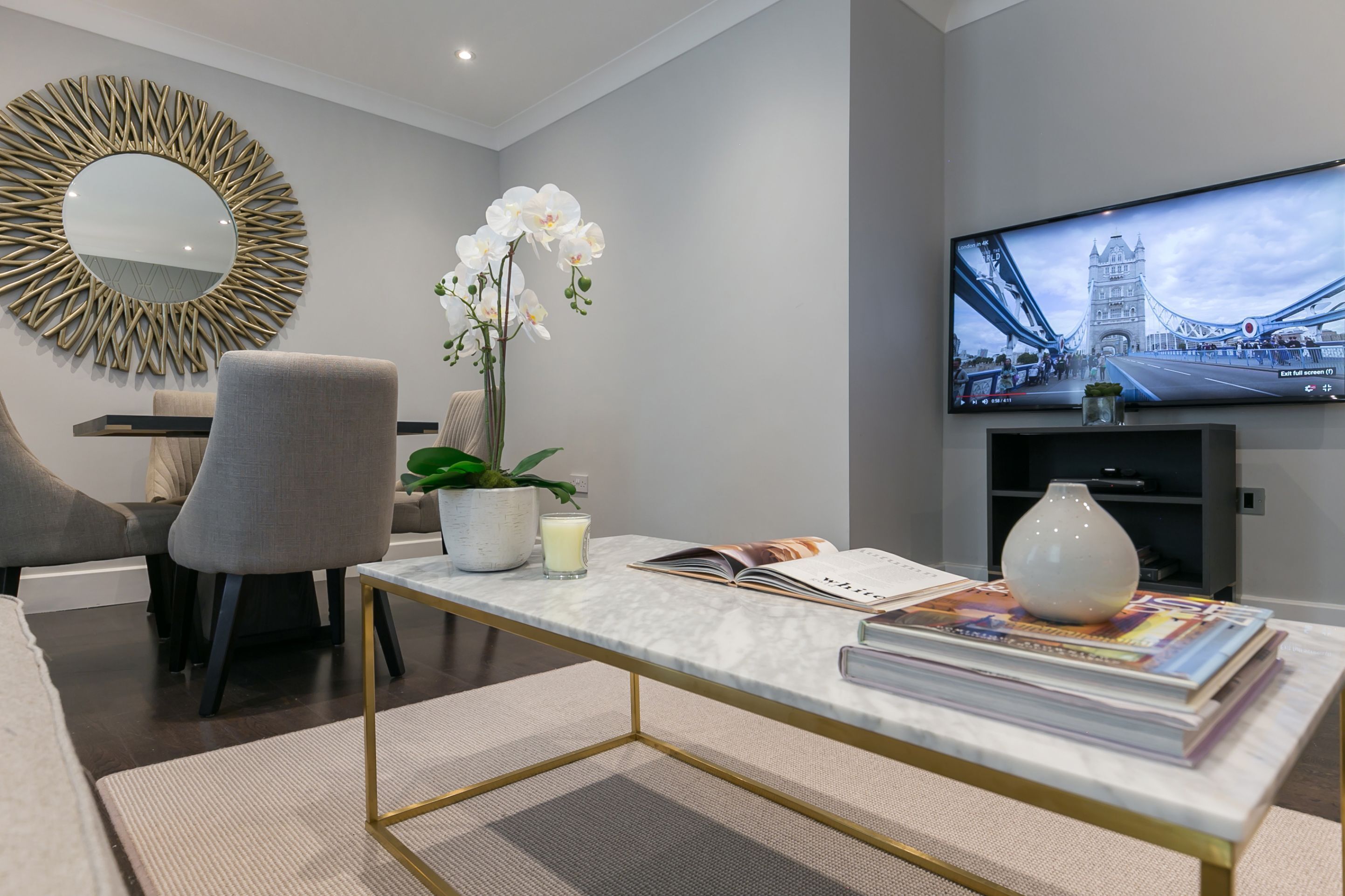 A modern living room with a television displaying a bridge, a comfortable sofa, a stylish coffee table, and decorative elements like an orchid and a vase.