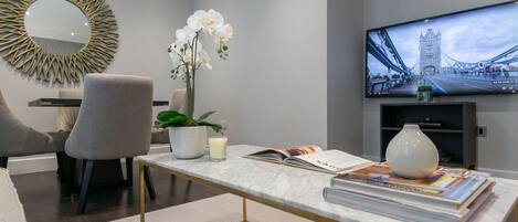 A modern living room with a television displaying a bridge, a comfortable sofa, a stylish coffee table, and decorative elements like an orchid and a vase.