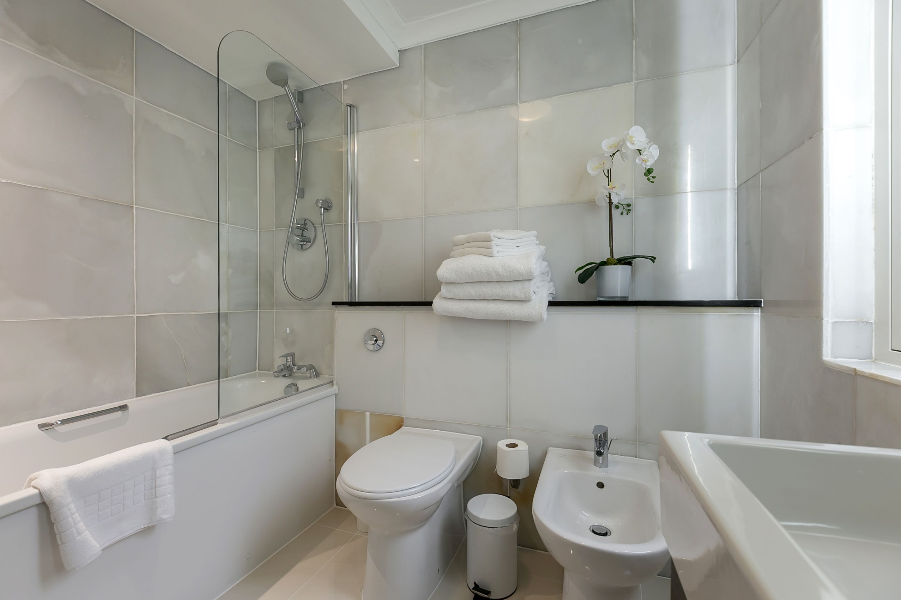 Une salle de bain moderne dotée d’une douche à parois de verre, de toilettes, d’un bidet, d’un lavabo et d’un miroir.