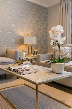 A modern living room with a geometric-patterned wall, a white sofa, a coffee table with a book and a lamp, and a potted orchid plant.