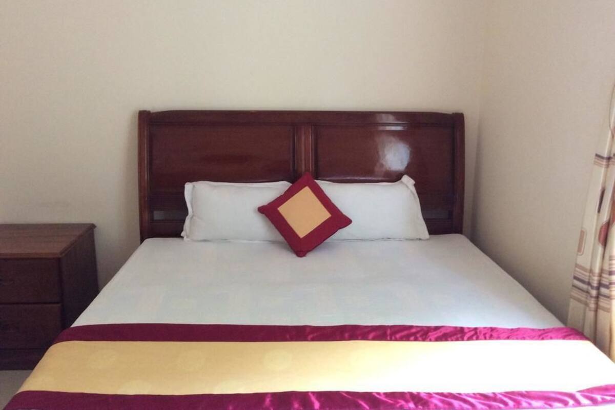 A neatly made bed with a wooden headboard, a white pillow, and a red and yellow throw blanket.