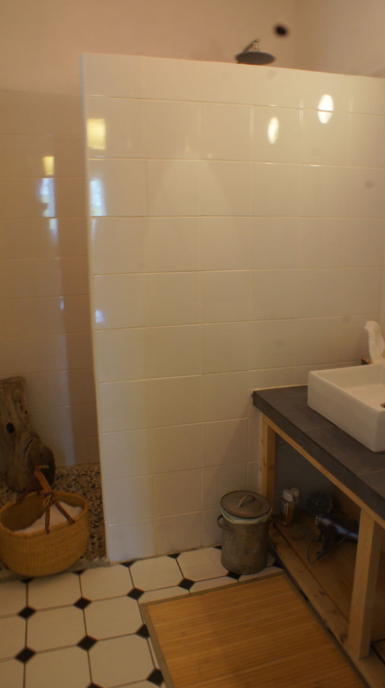A bathroom with white tiles, a wooden floor, a sink, and a trash bin.