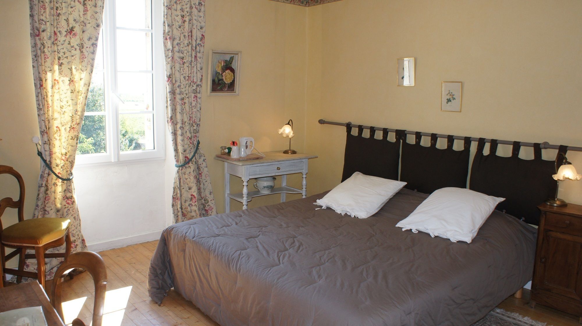 A bedroom with a bed, a nightstand, a small table, a chair, and a window with curtains.