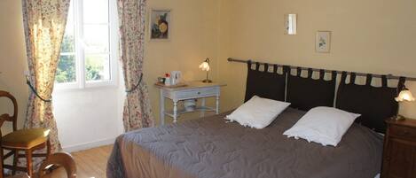 A bedroom with a bed, a nightstand, a small table, a chair, and a window with curtains.