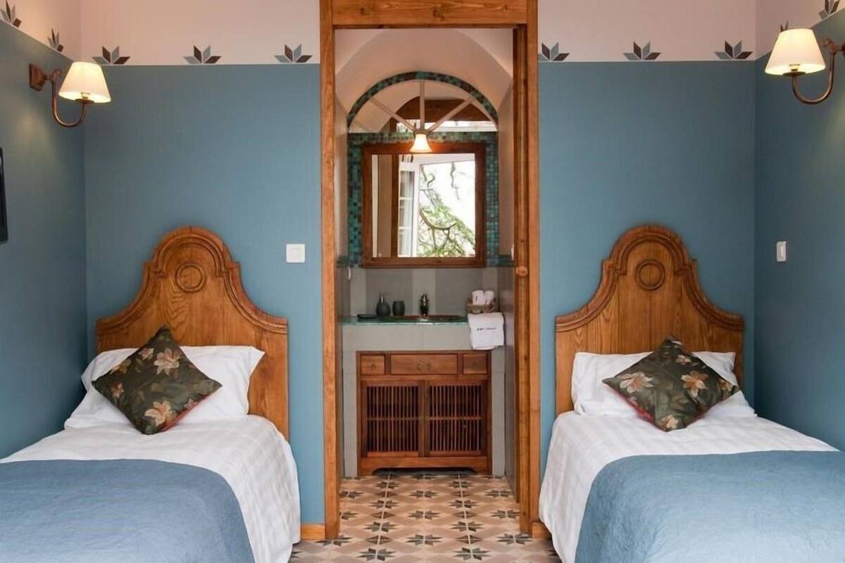 A room with two beds, a wooden dresser, a mirror, and a tiled floor.