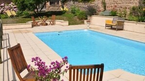 A rectangular swimming pool with a tiled deck, surrounded by outdoor furniture and greenery. - Les Jardins de L'hacienda (Tarare)