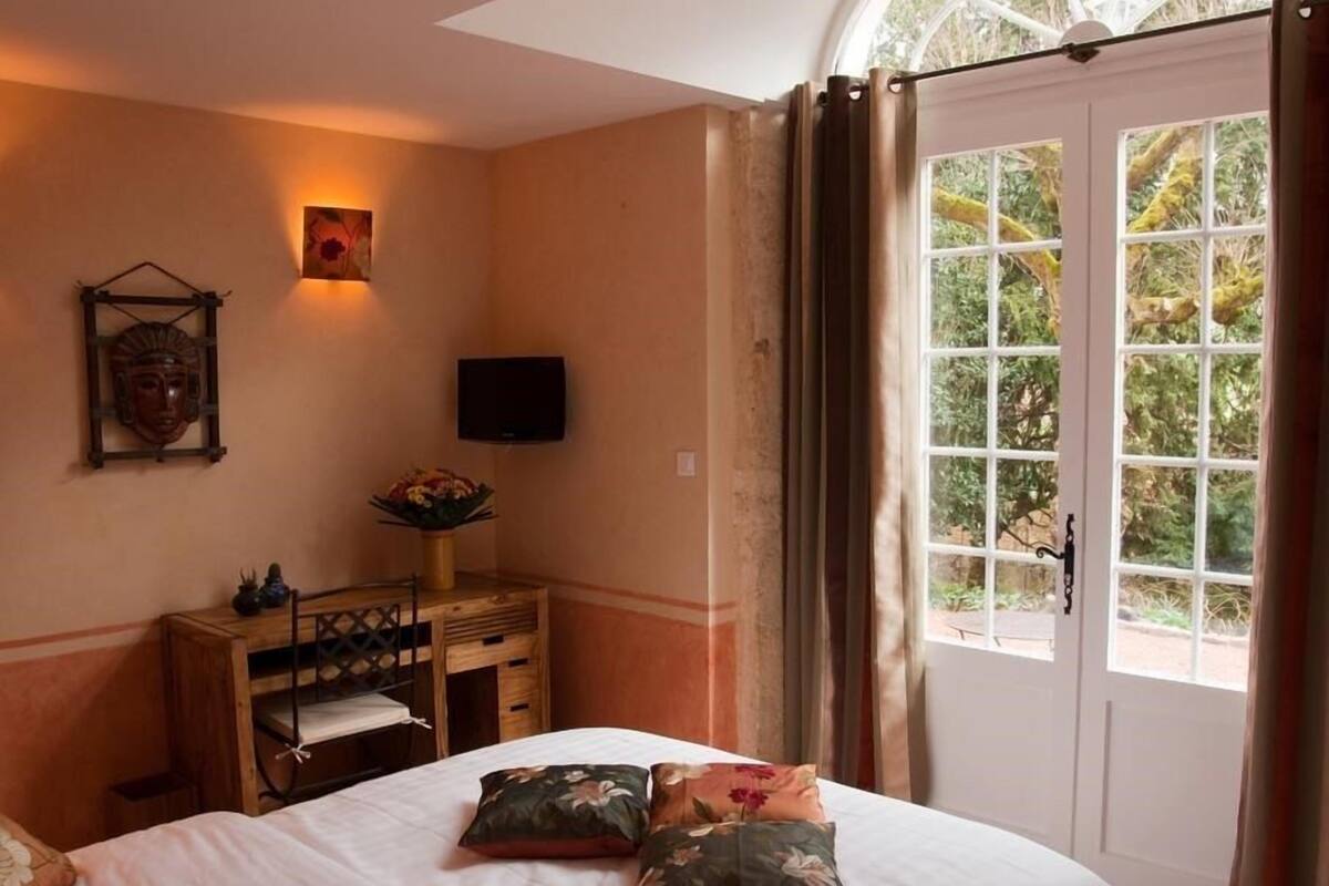 A bedroom with a bed, a desk, a chair, a TV, and a window with curtains.