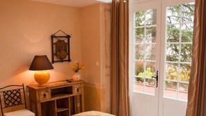 A bedroom with a bed, a nightstand, a lamp, a chair, a desk, and a window with curtains. - Les Jardins de L'hacienda (Tarare)