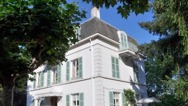 A white building with green shutters, a balcony, and a statue in front. - Les Jardins de L'hacienda (Tarare)