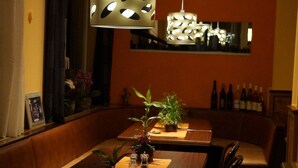 Un comedor con una larga mesa, múltiples sillas, plantas en macetas e iluminación colgante.