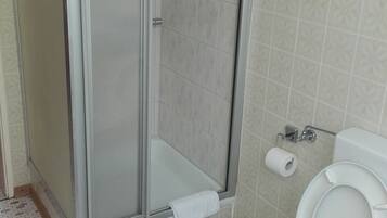 Baño con cabina de ducha, inodoro y baldosas de suelo estampadas.