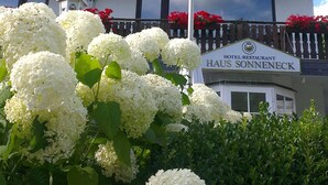 Un hotel con un balcón decorado con flores rojas, un letrero que dice "HOTEL-RESTAURANT HAUS SONNENECK" y un asta de bandera.