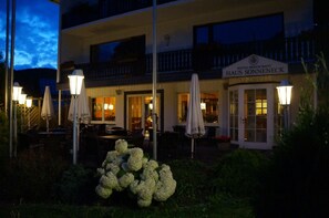 A hotel with outdoor seating and umbrellas, a sign reading "HAUS SONNEBECK," and a well-lit entrance. - Sonneneck (Winterberg)