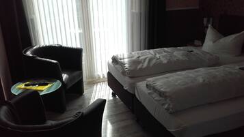 Habitación de hotel con cama, una silla, una mesita y una ventana con persianas.