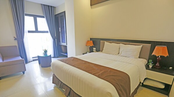 Habitación de hotel con cama, mesita de noche con lámparas, una silla y ventana con cortinas.