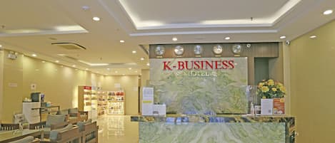A K-Business Hotel reception area with a marble counter, seating area, and a display of amenities.