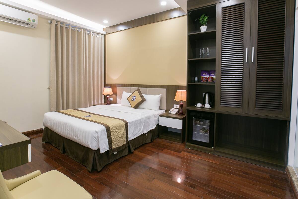 A hotel room with a bed, bedside lamps, a wardrobe, a desk, and a chair.