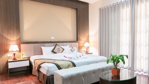A hotel room with a large bed, bedside tables with lamps, a glass coffee table, and a potted plant. - Blubiz Hotel My Dinh Song Da (Hanoi)