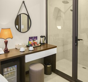 Baño de hotel con ducha, espejo, cafetera y artículos de aseo en la encimera.