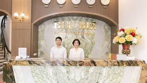 A hotel reception desk with a marble top, clocks displaying different cities, and a floral arrangement. - Blubiz Hotel My Dinh Song Da (Hanoi)