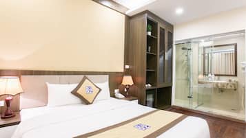 A hotel room with a bed, bedside lamps, a nightstand, a glass-enclosed shower, and a wooden wardrobe.