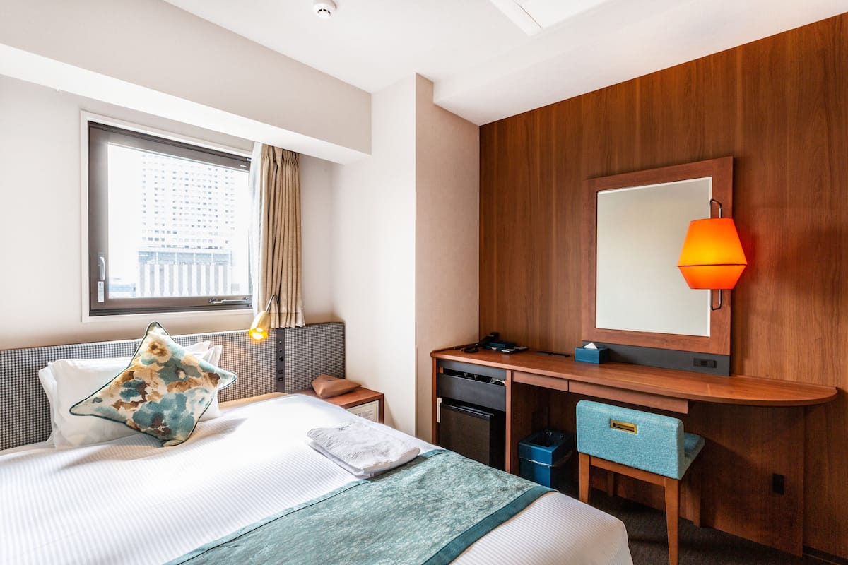 A hotel room with a bed, a desk, a mirror, and a window with curtains.