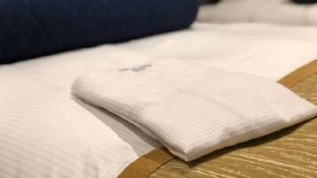 A neatly made bed with white and brown bedding, a folded white towel, and a blue pillow.