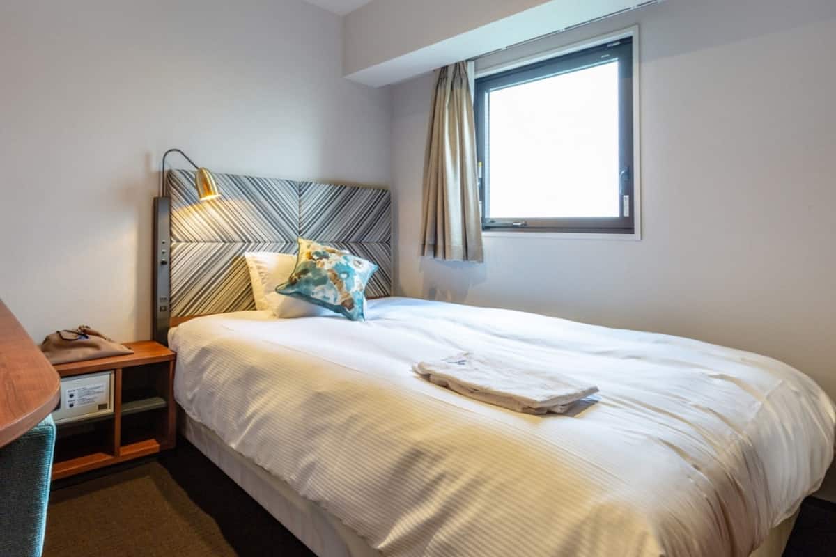 A hotel room with a bed, a nightstand, a desk, and a window with curtains.