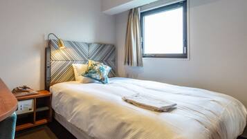 A hotel room with a bed, a nightstand, a desk, and a window with curtains.