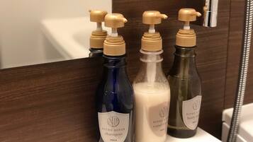 A bathroom with a mirror, a shelf holding three bottles of shampoo, and a black and white checkered towel.