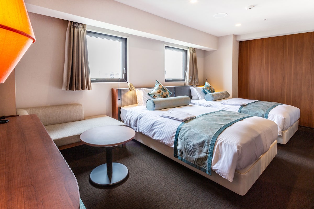 A hotel room with two beds, a sofa, a small round table, and a lamp.