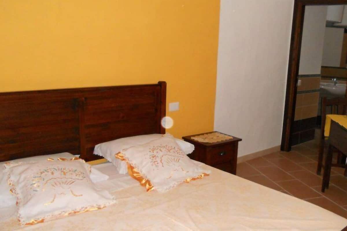 A bedroom with two beds, a wooden headboard, a nightstand, a table with a yellow tablecloth, and a chair.