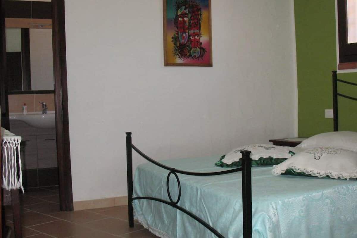 A bedroom with a bed, a nightstand, a chair, a window, and a painting on the wall.