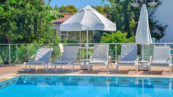 Una piscina al aire libre, sombrillas, sillones reclinables de piscina