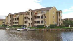 A multi-story residential building with balconies, a dock with a boat, and a calm water body in front. - Seascape-heron Harbour 204-4 2 Bedroom Condo by RedAwning (Ocean City)