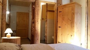 A rustic wooden room with a bed, a wooden wardrobe, and a door leading to a bathroom. - Chambres d'Hôtes La Fée Verte (Arc-sous-Cicon)