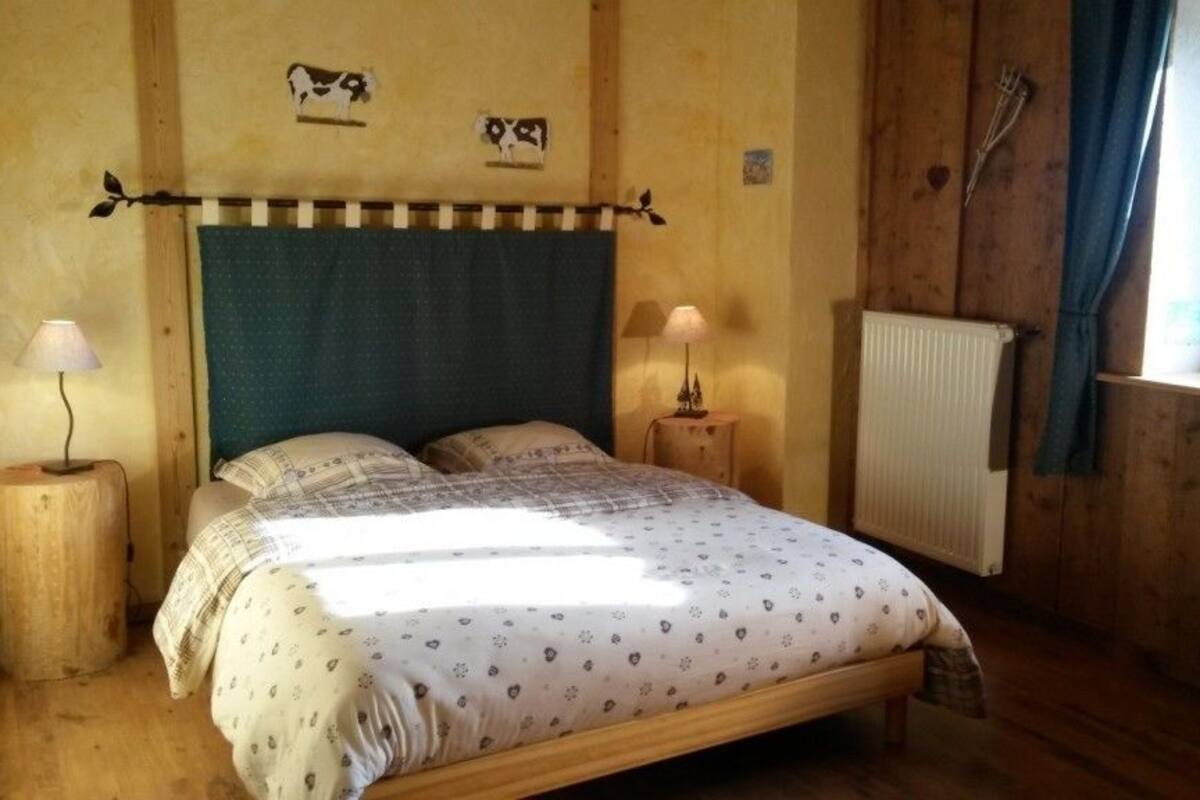 Ein Schlafzimmer mit Holzrahmen, einem Bett, zwei Nachttischlampen, einem Heizkörper und einem Fenster mit Vorhängen.
