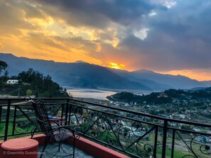A balcony with a chair and a small table, overlooking a valley with mountains and a river. - Greenhills Guesthouse (Pokhara)
