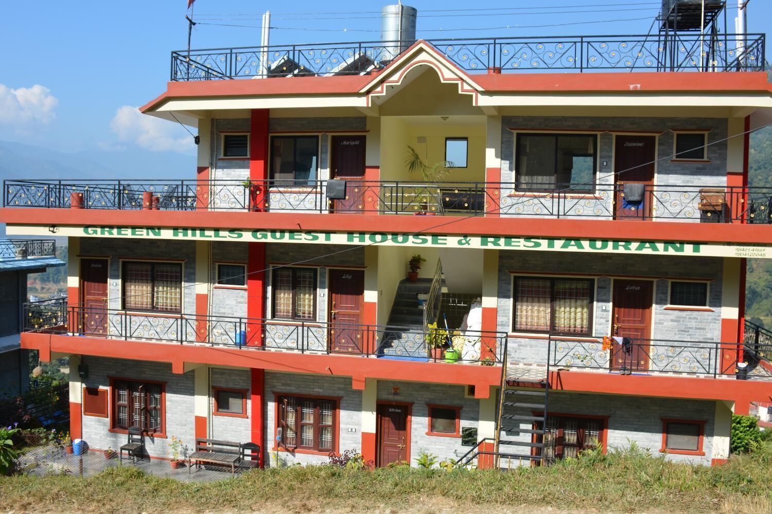 A two-story building with balconies, a sign reading "GREEN HILLS GUEST HOUSE & RESTAURANT", and a staircase leading to the upper floor.