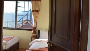 A hotel room with two beds, a wooden door labeled "Marigold," a ceiling fan, and a window with a view of buildings and mountains.