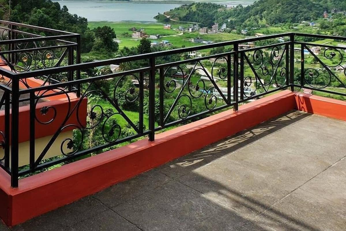 Ein Balkon mit Metallgeländer, der auf ein Tal mit Fluss und verstreuten Gebäuden blickt.
