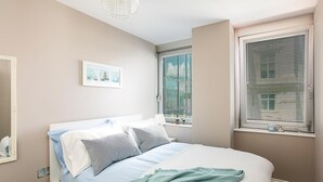 A bedroom with a bed, a window with blinds, a chandelier, and a framed picture on the wall. - Green Diamond by Creatick Apartments (Brighton)