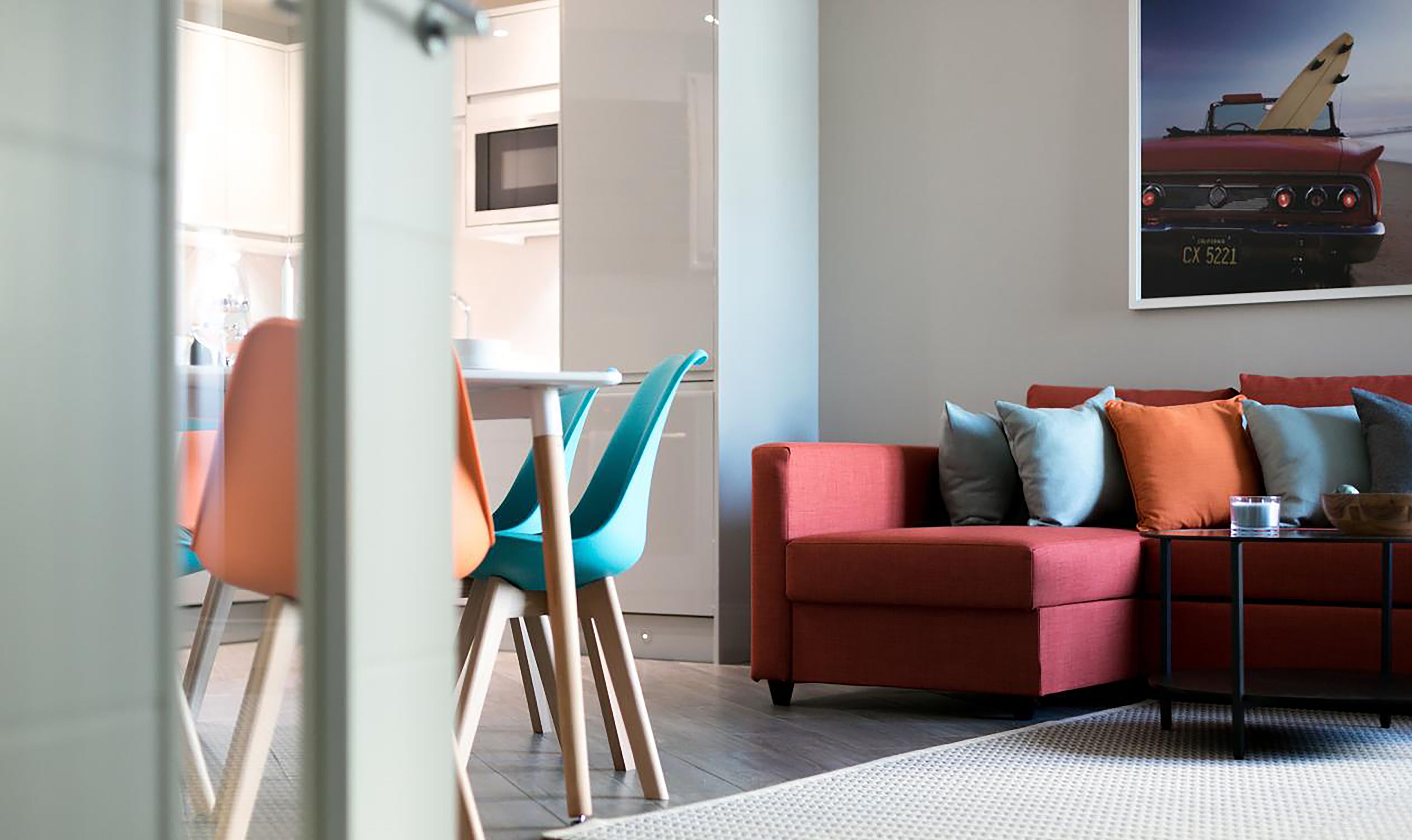 Un salon moderne avec un canapé rouge, des fauteuils turquoise et une table basse en verre.