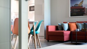 A modern living room with a red sofa, teal chairs, and a glass coffee table. - Green Diamond by Creatick Apartments (Brighton)
