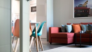 A modern living room with a red sofa, teal chairs, and a glass coffee table. - Green Diamond by Creatick Apartments (Brighton)