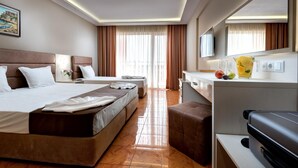 A hotel room with two beds, a desk, a chair, a suitcase, and a large window with curtains. - Hotel Sunny (Sozopol)